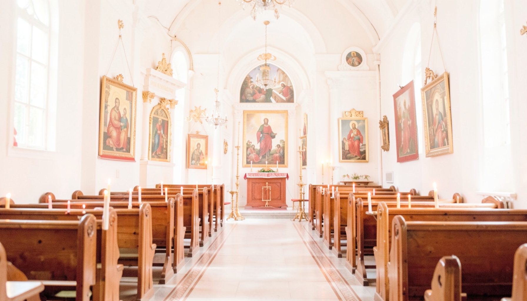 A bright, airy photograph of an Orthodox church interior with warm candlelight, gold-toned icons, and wooden pews, creating a reverent and serene atmosphere.